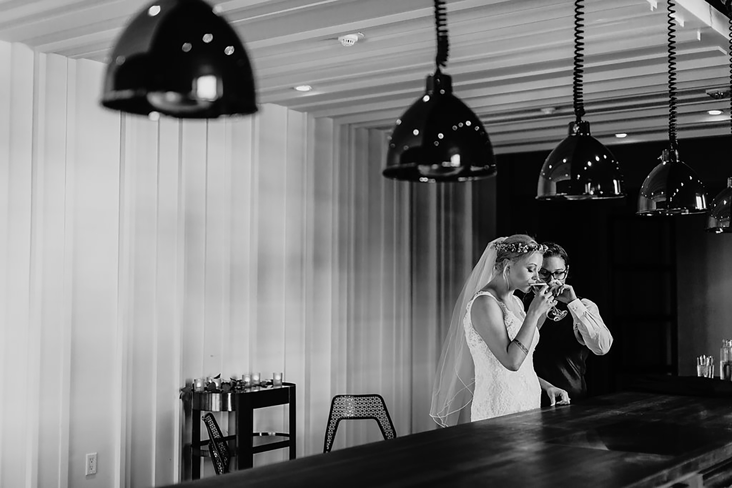 black and white photo of bride and bride drinking cocktails at bar