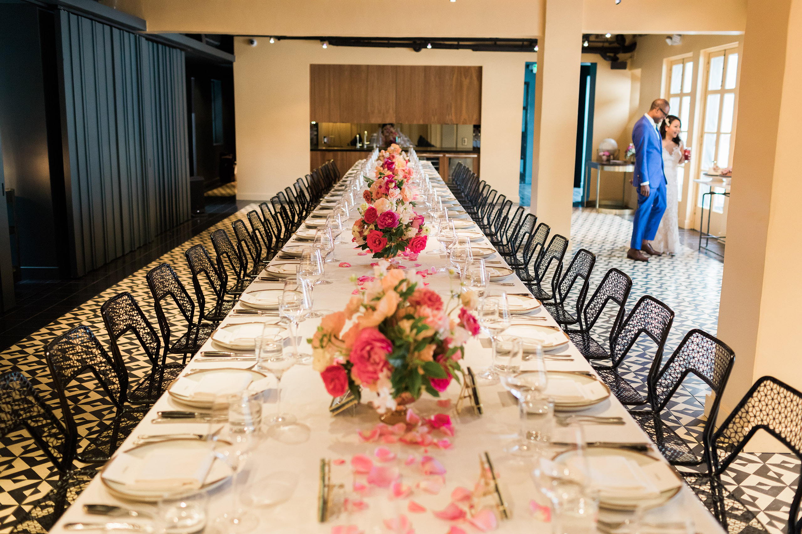 interior dining room with single long table set with flowers and bride and groom in the background