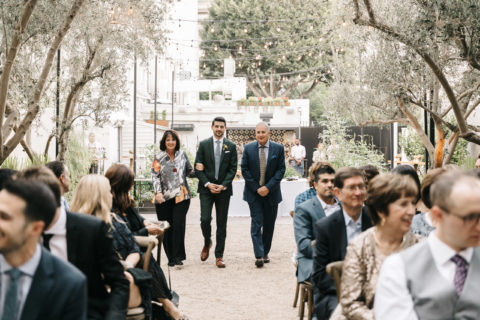 wedding with guests seated while groom walks down aisle with mom and dad