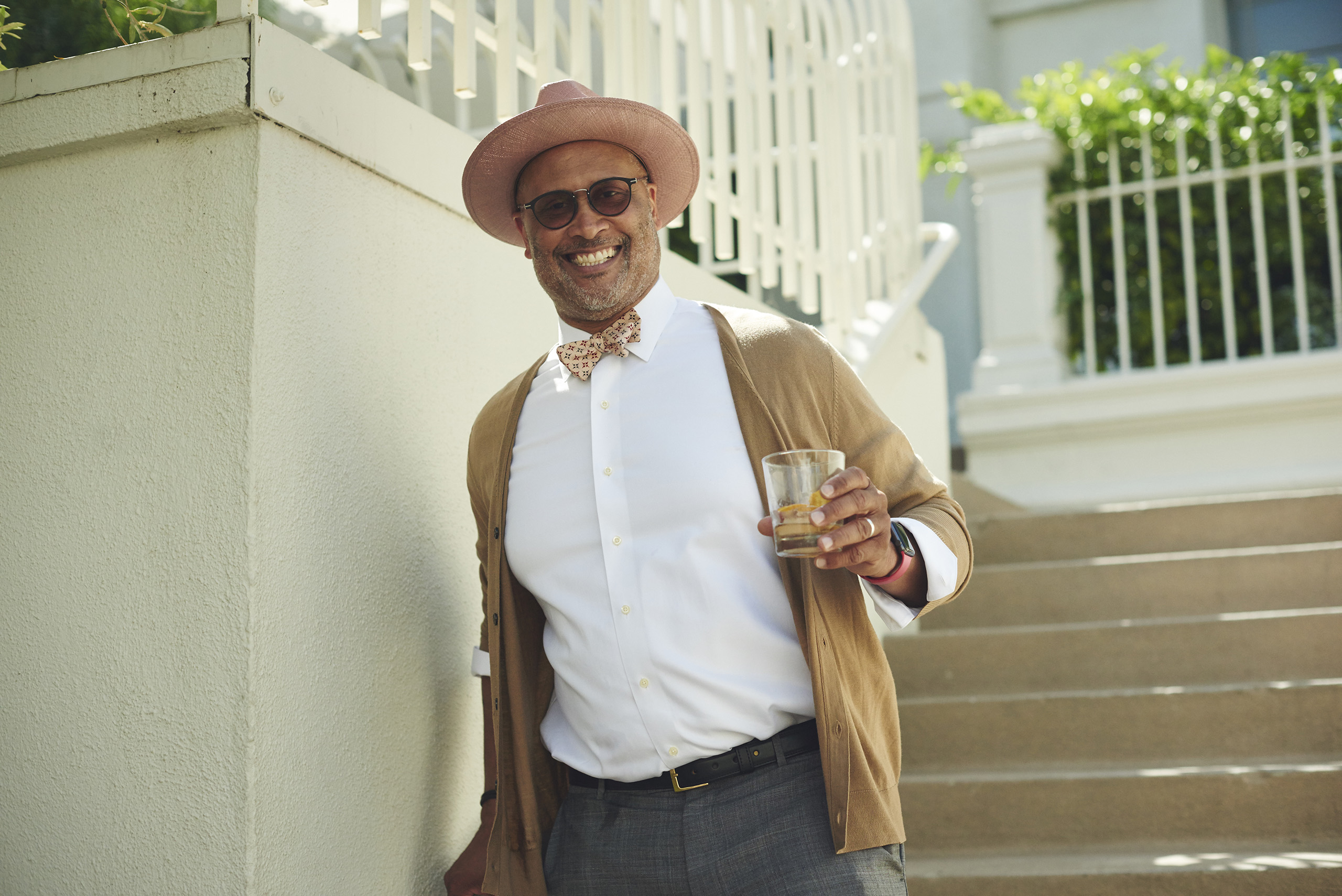 smiling man in white Oxford and peach hat and camel cardigan