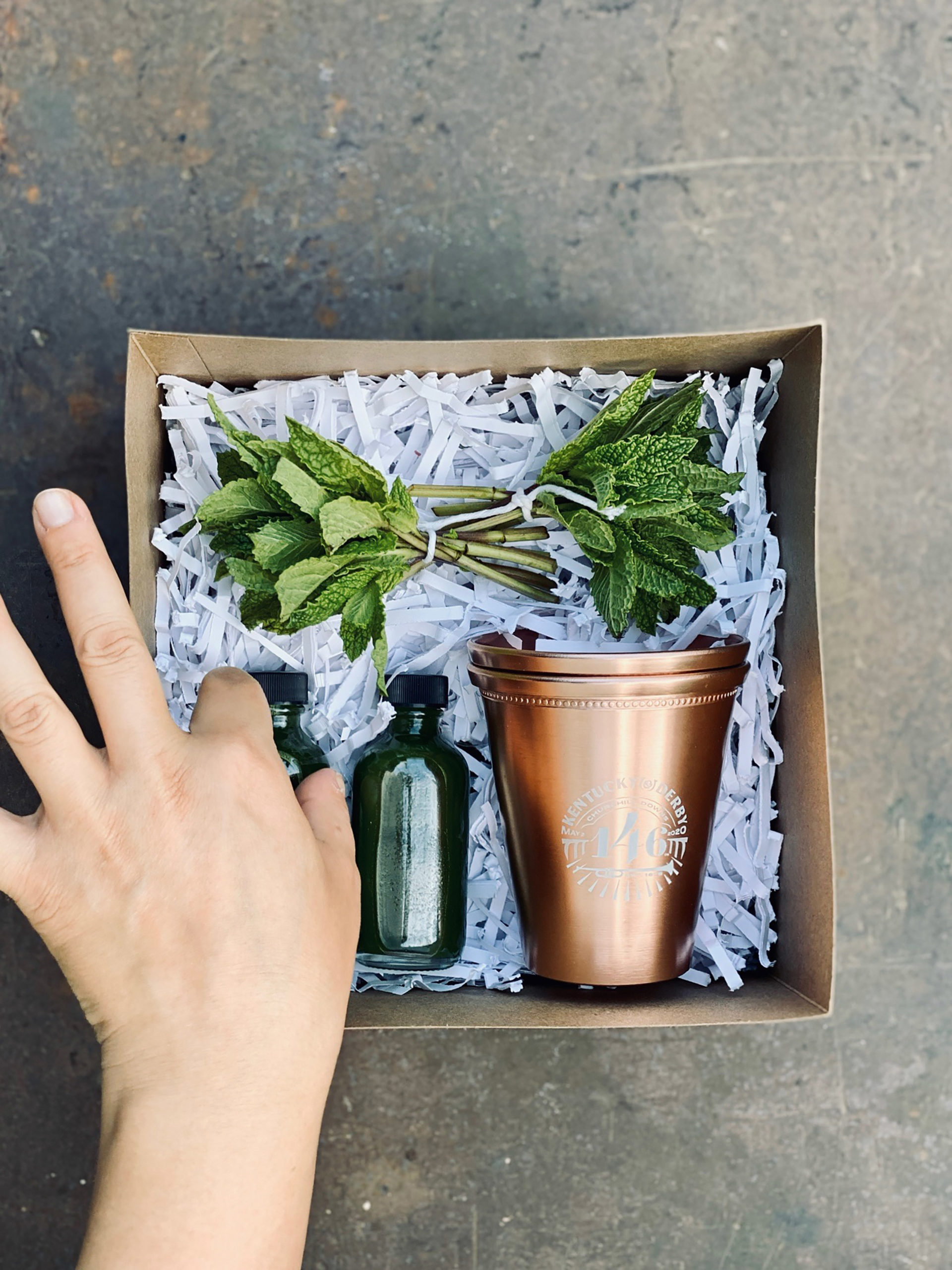 box with hand reaching in inside is mint and 2 green bottles and copper glasses