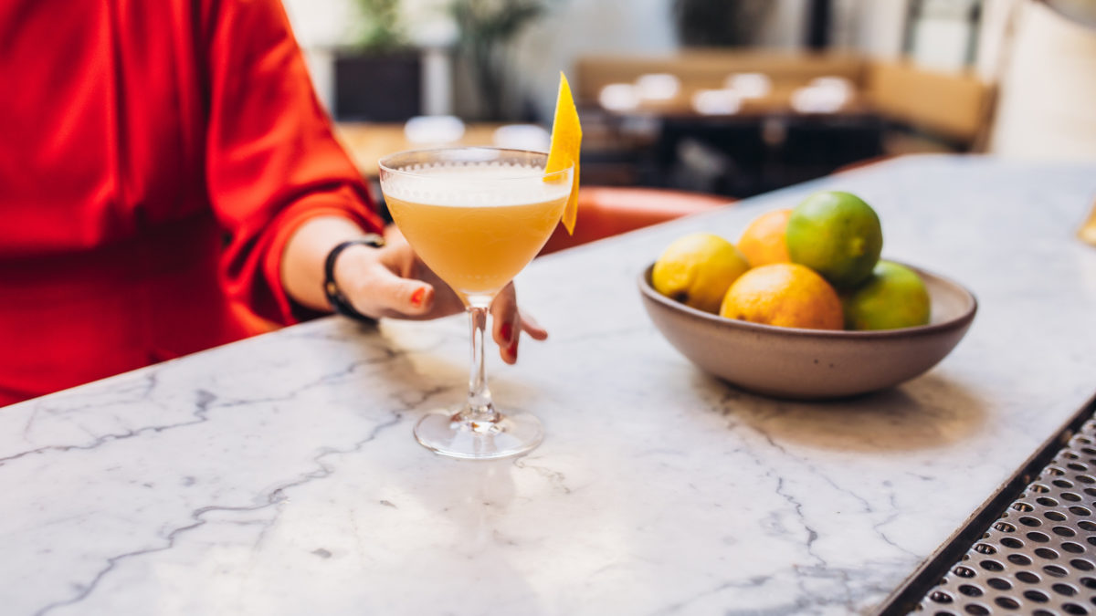 woman in red dress holding cocktail with lemon peel on top at bar in coup glass