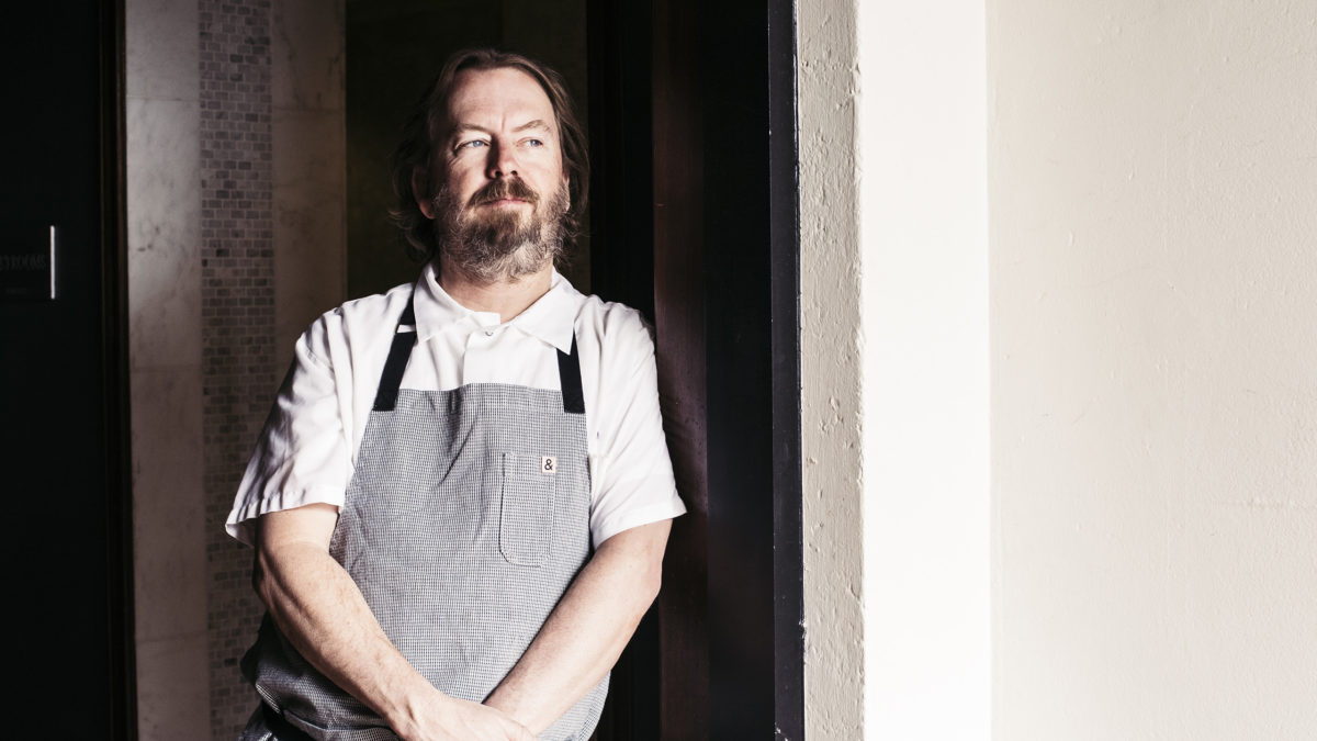Neal Fraser leaning against wall in grey apron