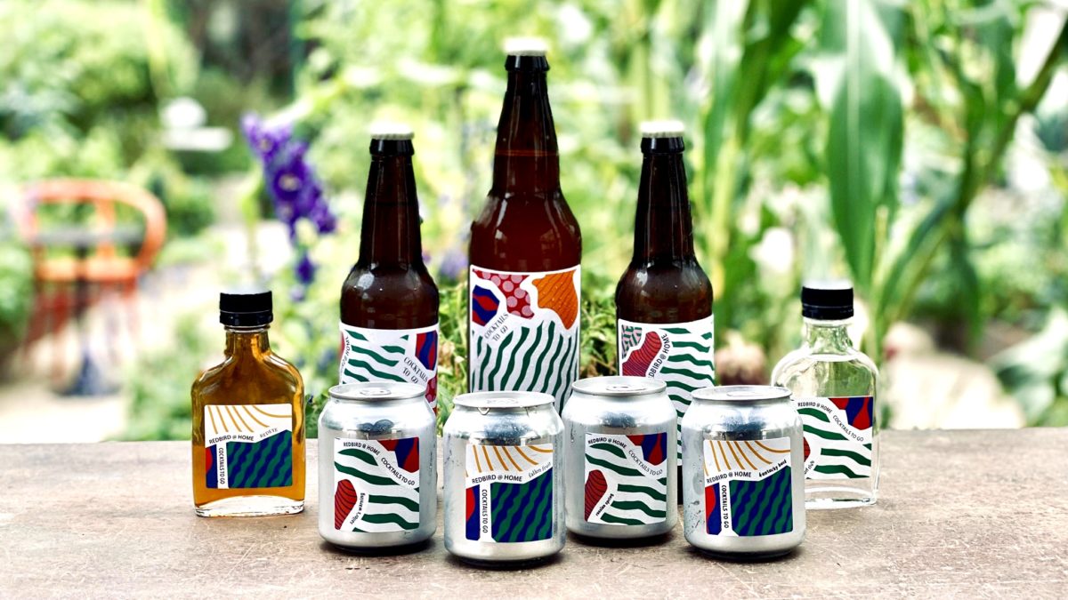 bottled of cocktails with funky labels sitting on a table with garden in background