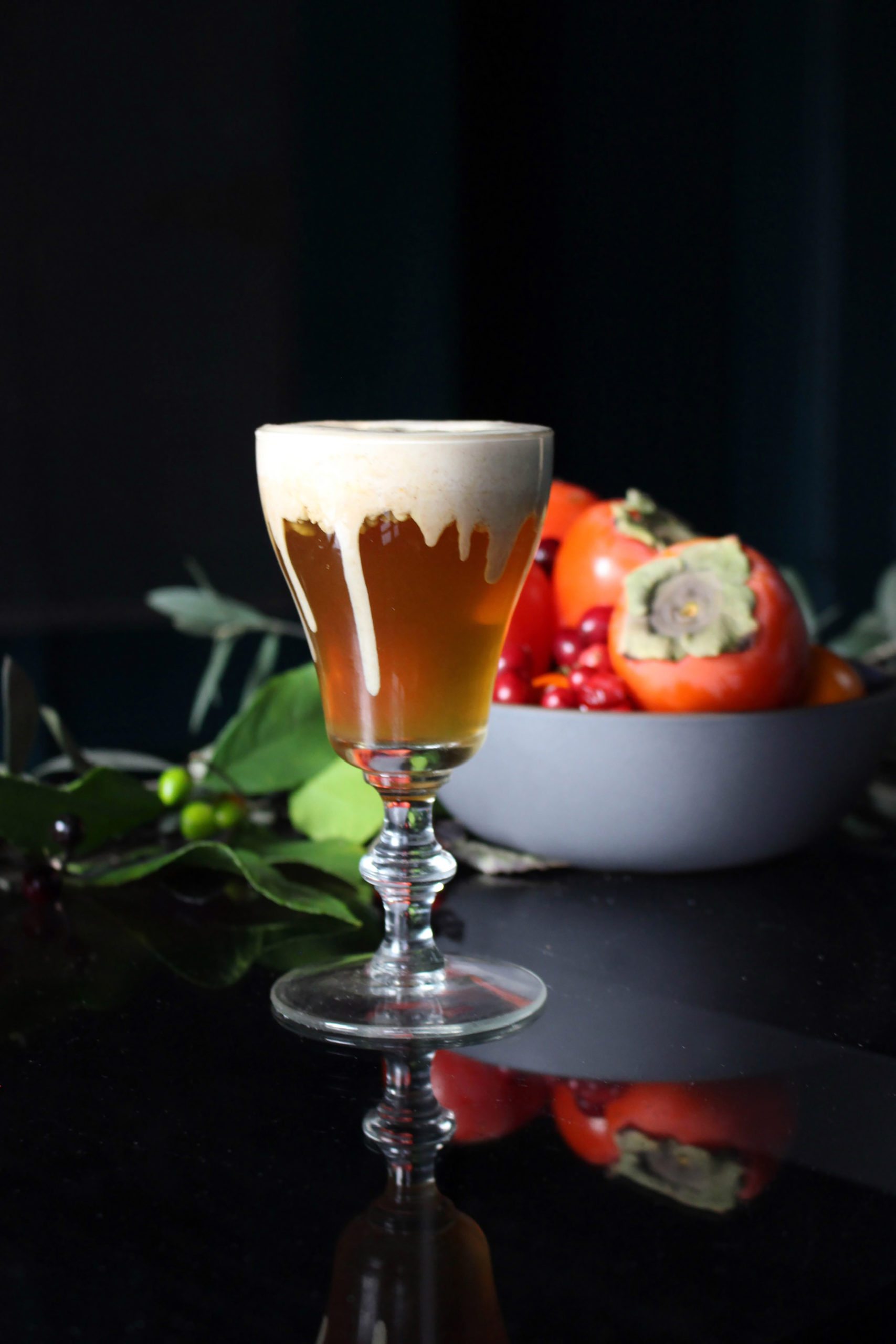 foam dripping down cocktail dramatically with persimmon in background