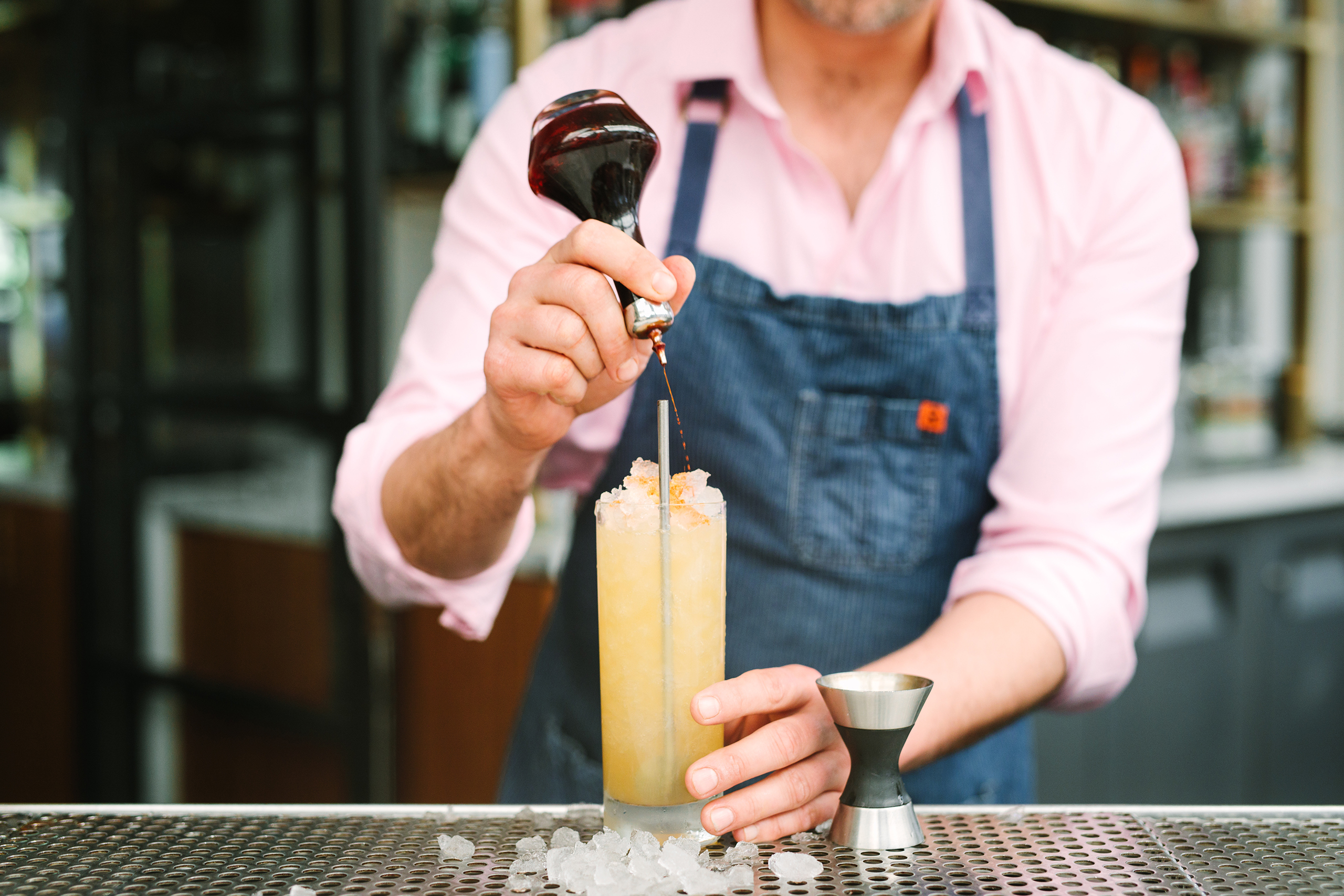 bartender making yellow cocktail with blue apron and pink shirt