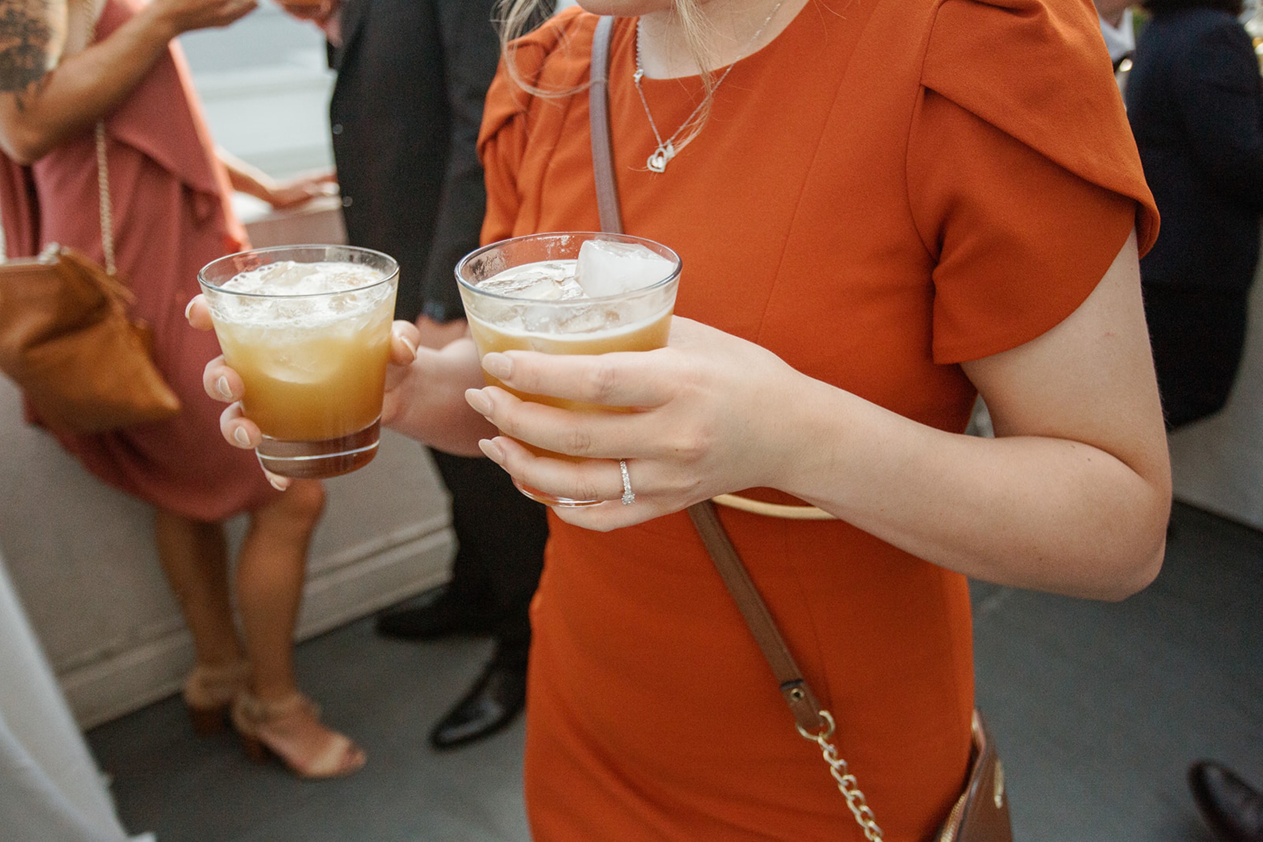 woman in orange dress holding 2 cocktails
