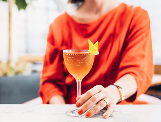 woman with orange nails and dress holding an orange cocktail