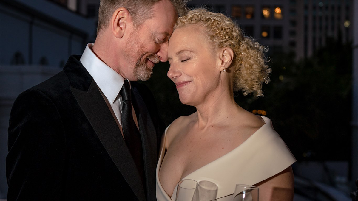 a bride and groom sharing an intimate moment on outdoor patio in front of skyline holding champagne