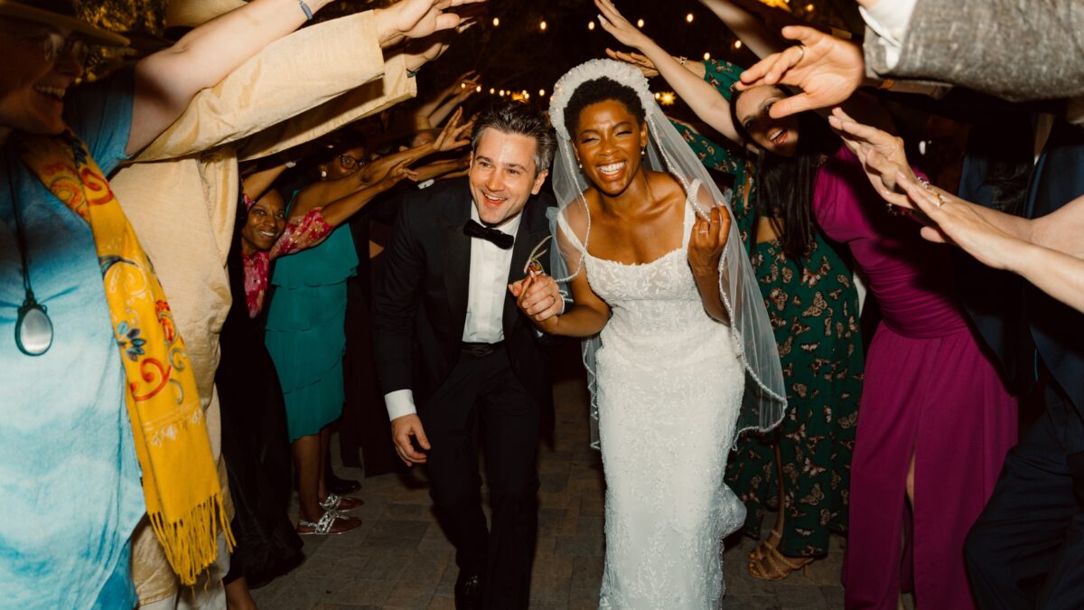 a bride and groom make their way through a tunnel made by guests raising their arms